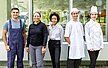 Ein Teamfoto mit verschiedenen Mitarbeitenden: einem Hausmeister, zwei Verwaltungsangestellten und zwei Mitarbeitenden aus der Gastronomie