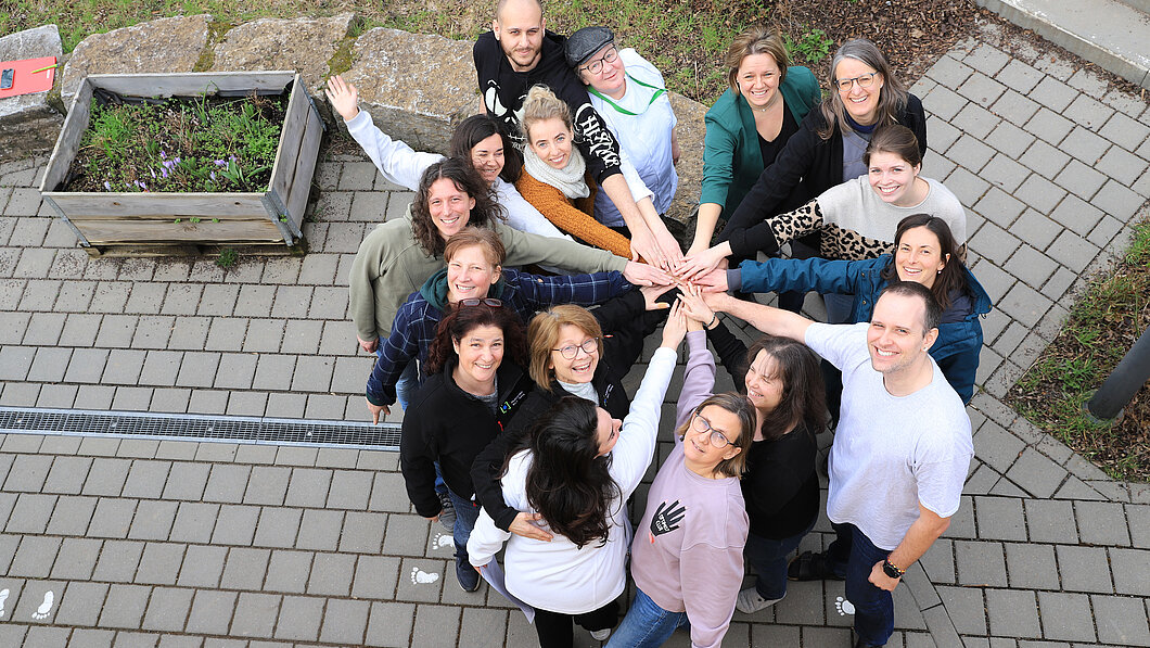 Bild von oben fotografiert auf das Team der Campus-Kita Mainz, die die Hände im Kreis zusammenhalten - Teamwork
