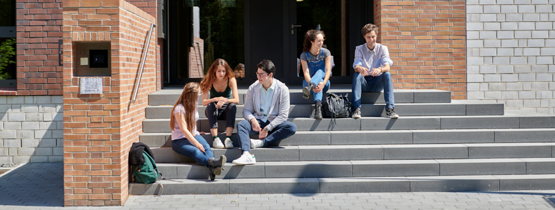 Fünf Personen sitzen auf der Treppe vor einem Wohnheim