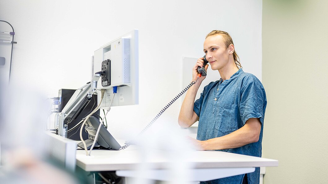 Mitarbeitender steht an seinem Stehtisch und telefoniert