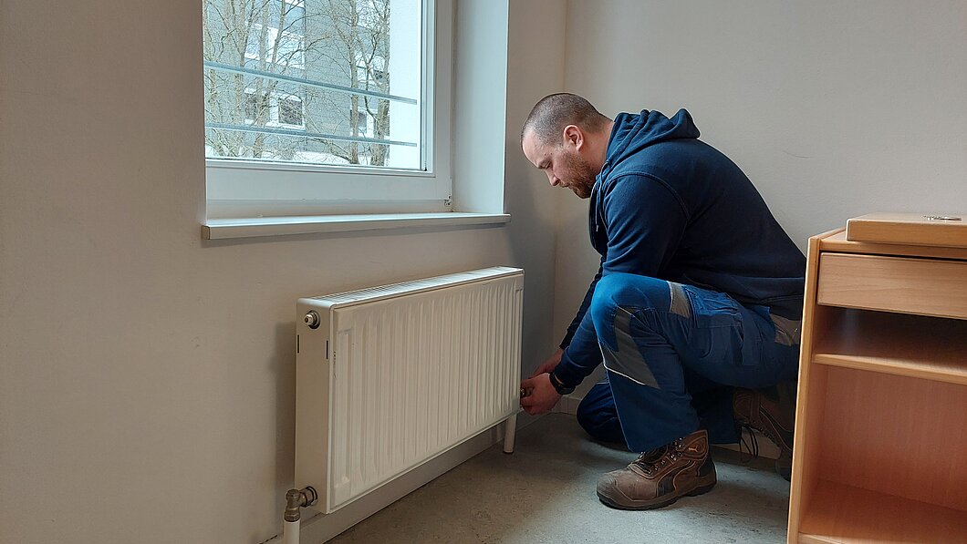 Hausmeister repariert Heizung in einem WG Zimmer