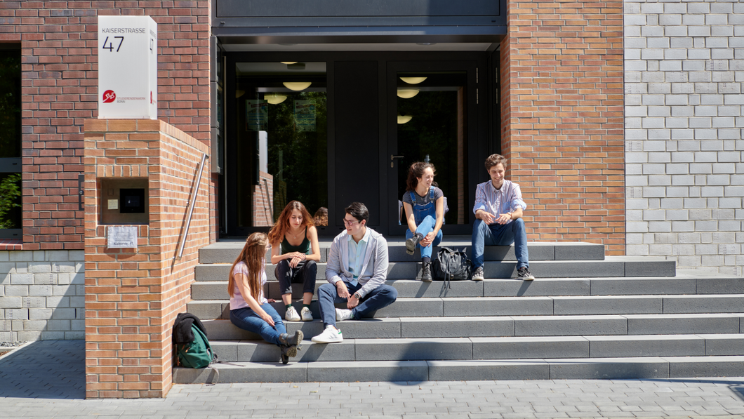 Eine Gruppe Studierender sitzt auf den Stufen, die zum Wohnheim Kaiserstraße führen.