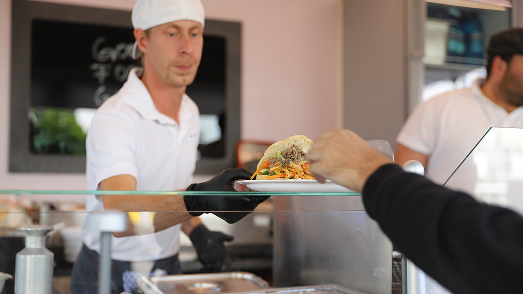 Foto auf dem ein Mitarbeiter Essen aus dem Food-Truck an einen Studierenden ausgibt