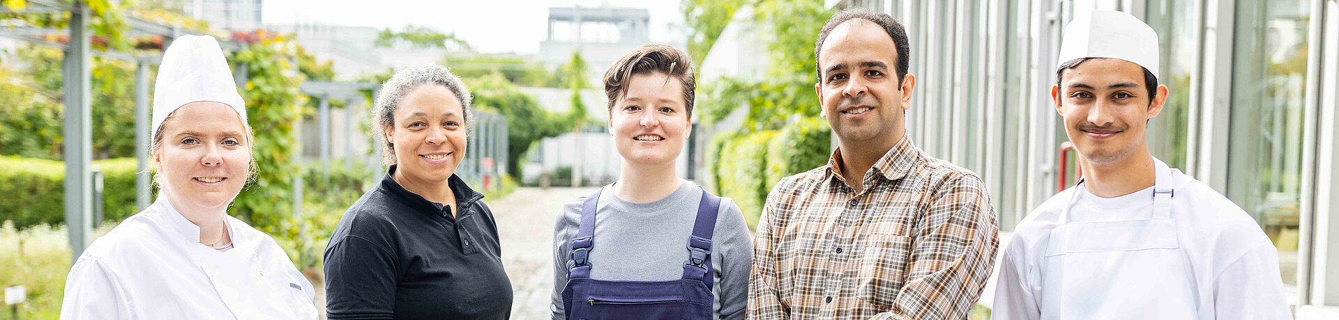 Ein Teamfoto mit verschiedenen Mitarbeitenden: einem Hausmeister, zwei Verwaltungsangestellten und zwei Mitarbeitenden aus der Gastronomie
