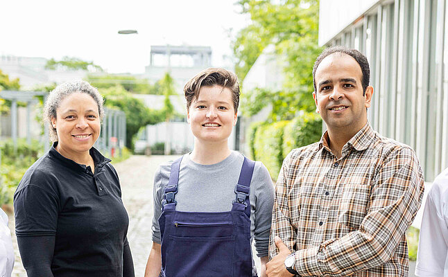 Ein Teamfoto mit verschiedenen Mitarbeitenden: einem Hausmeister, zwei Verwaltungsangestellten und zwei Mitarbeitenden aus der Gastronomie