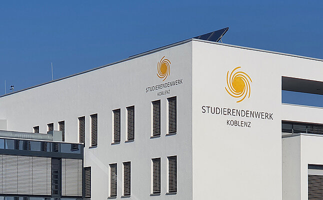 Ein weißes Gebäude mit dem Logo des Studierendenwerks Koblenz vor Blauem Himmel